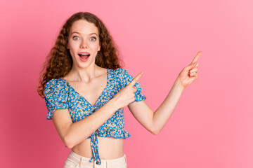 Excited woman pointing with surprise on a pink background