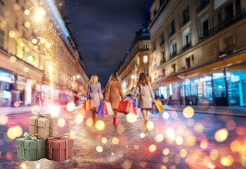 Blurry lights and bokeh illuminate a Parisian street at night with women shopping and carrying bags.