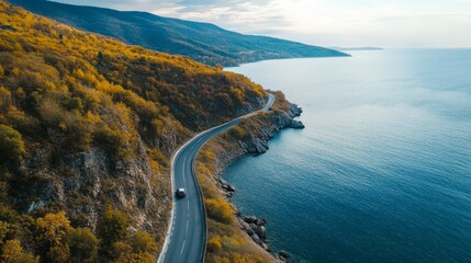 Obraz premium Aerial Drone View of a Car Driving Along an Autumn Mountain Road Near the Sea, Showcasing Stunning Autumn Forest Landscape and Nature Scenery in a Fall Countryside Setting.