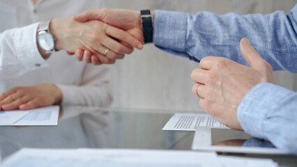 Business people shaking hands over contract agreement and financial papers at the glass table. Professional handshake, close up