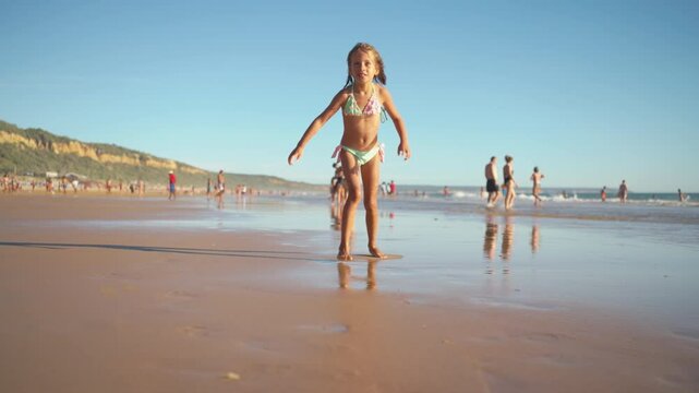 Cheerful wet girl running on sandy beach against clear blue sky during sunny day. Female child in swimwear is spending leisure time during vacation 