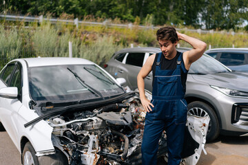 Pondering mechanic scratching head in frustration while assessing damage on car after an accident....