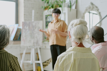 Obraz premium Back view shot of unrecognizable biracial students listening to teacher carefully in modern drawing studio