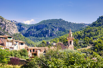 Vista panor&aacute;mica de un pintoresco pueblo rodeado de monta&ntilde;as y vegetaci&oacute;n, con una iglesia destac&aacute;ndose entre los edificios bajo un cielo despejado. Ideal para transmitir tranquilidad y belleza rural.
