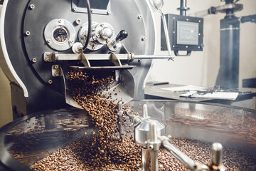 Filling out of freshly roasted coffee beans from large coffee roaster into cooling cylinder.