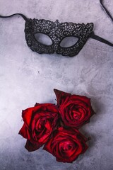 Black masquerade mask made of lace and three roses on a gray background