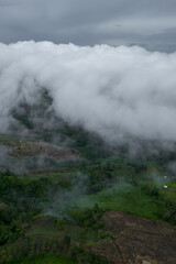 A stunning aerial photograph capturing lush green hills and valleys enveloped in misty clouds, creating a serene and mystical atmosphere.