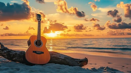 A brown acoustic guitar rests on a weathered piece of driftwood on a sandy beach with the setting sun and ocean in the background.