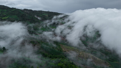 A stunning aerial shot capturing lush green hills and valleys shrouded in misty clouds, creating a serene and mystical landscape.