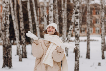 Happy smiling young woman portrait dressed coat scarf hat and mittens enjoys winter weather at birch winter park