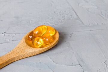 Vitamin omega capsules in a spoon on a colored background. Pills served as a healthy meal. Red soft...