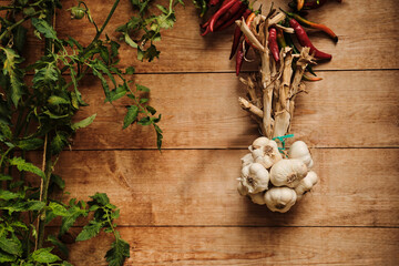 Fresh garlic cloves hanging on rustic wooden background with green tomato plant and red chilli peppers. Perfect for food, cooking, and healthy lifestyle concepts.