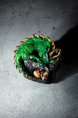 A green dragon with golden spikes sitting on a large stone. Figurine of the symbol of 2025. Dark...