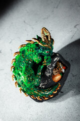 A green dragon with golden spikes sitting on a large stone. Figurine of the symbol of 2025. Dark...
