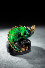 A green dragon with golden spikes sitting on a large stone. Figurine of the symbol of 2025. Dark...