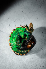 A green dragon with golden spikes sitting on a large stone. Figurine of the symbol of 2025. Dark...