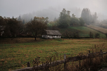 A solitary wooden house nestled in a misty, forested valley. The scene evokes a sense of...