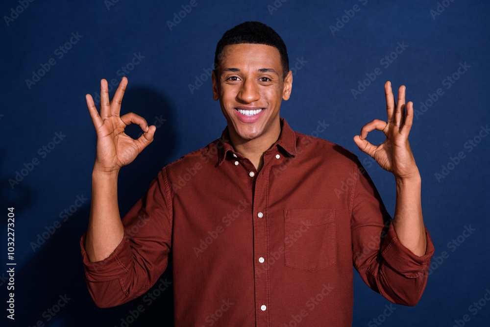 Wall mural Photo portrait of handsome young man show double okey dressed stylish brown garment isolated on dark blue color background