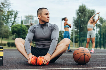 Attractive, Asian man wearing sportwear warming up sitting on the street, training, doing exercise