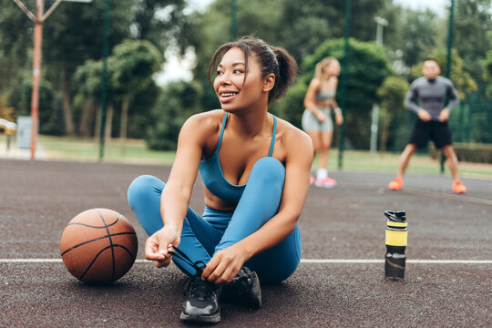 Smiling, African American woman tie shoelaces preparing playing basketball on the street, outdoors