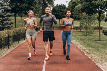 Diverse group of happy, active sportswomen and handsome coach wearing stylish sportwear running