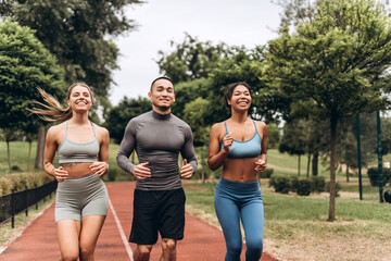 Multinational sportspeople wearing stylish sportwear running together, training on the street