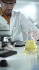 Man scientist wearing white protective gloves, and glasses is holding a yellow chemical solution...