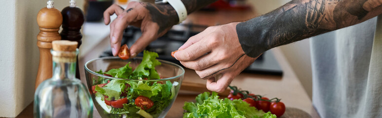 A young, handsome man skillfully mixes fresh vegetables in a bowl while cooking at home.