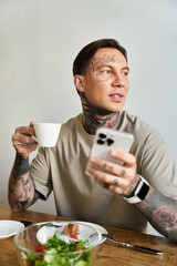 A young man sips coffee and checks his smartphone, surrounded by a fresh salad at home.