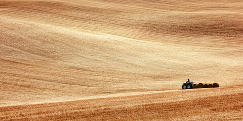 Obraz premium A tractor pulls compacted hay runoff across a rural field. Hay collection and processing, farming season, village