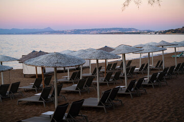 Empty row of sunshade and sunbed on beach in sunset warm lighting. Kato Stalos, Crete, Greece
