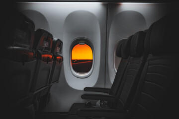 View from an airplane window showcasing a stunning orange sunset on the horizon. The empty row of seats highlights the tranquility as the aircraft taxis on the runway, ready for takeoff.
