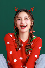 Young Beauty Asian happy woman wearing cozy red sweater dress and a reindeer antler hair clip gesture on green isolated background. winter, Happy new years concept.