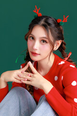 Naklejka premium Young Beauty Asian happy woman wearing cozy red sweater dress and a reindeer antler hair clip gesture on green isolated background. winter, Happy new years concept.