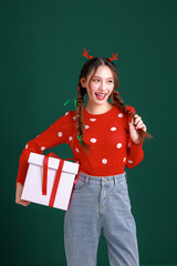 Young Beauty Asian happy woman wearing cozy red sweater dress and a reindeer antler hair clip holding gift boxes on green isolated background. winter, Happy new years concept.