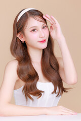 Fototapeta premium Pretty Asian beauty woman curly long hair with Korean makeup glowing face and healthy facial skin portrait smile on isolated beige background. Cosmetology ,Plastic surgery.