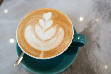 close up of milk coffee latte with heart and flower coffee art foam in a blue cup on a marble pattern table with a tea spoon