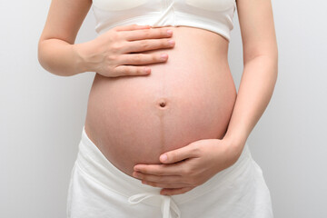 Pregnant woman hands cradling and holding her belly in white clothing.