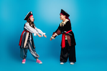 Full size photo of two small kids dancing halloween pirate costume isolated on blue color background