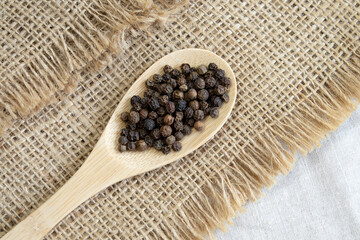 Pile of Black peppercorns Black pepper dried seeds in wooden spoon on linen background
