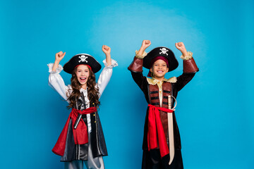 Portrait of two little kids halloween pirate costume raise fists isolated on blue color background