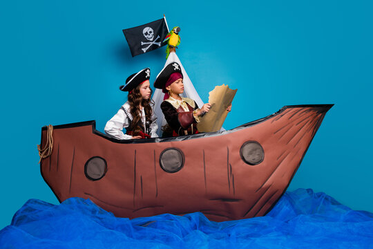 Full size photo of two little children hold map search treasure wear pirates halloween costumes ship decor isolated on blue background - Powered by Adobe