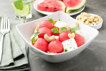 Delicious watermelon salad with feta cheese, cashew nuts and spices in bowl served on grey textured table, closeup