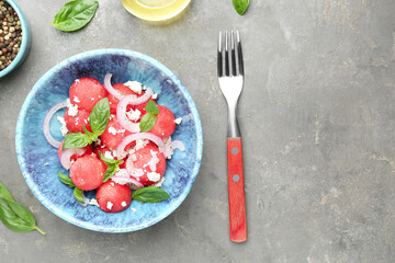 Delicious watermelon salad with feta cheese, mint and onion in bowl served on grey textured table, flat lay. Space for text
