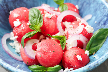 Delicious watermelon salad with feta cheese, mint and onion in bowl on table, closeup