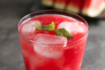 Tasty watermelon drink in glass and mint on blurred background, closeup