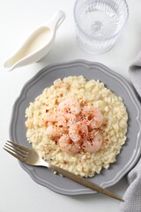 Delicious risotto with shrimps, cheese, sauce and water on white table, top view