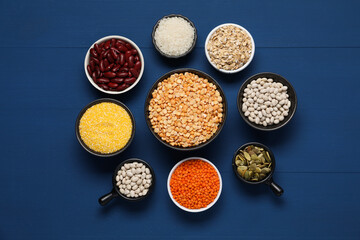 Different types of cereals, seeds and legumes on blue wooden table, flat lay