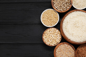 Different types of cereals and seeds in bowls on black wooden table, flat lay. Space for text