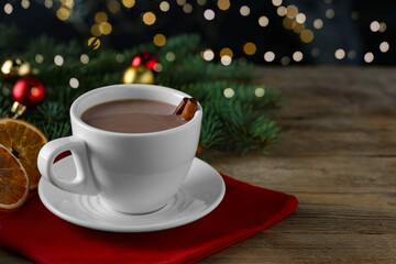 Tasty hot cocoa drink with cinnamon sticks in cup and dry orange slices on wooden table, closeup. Space for text